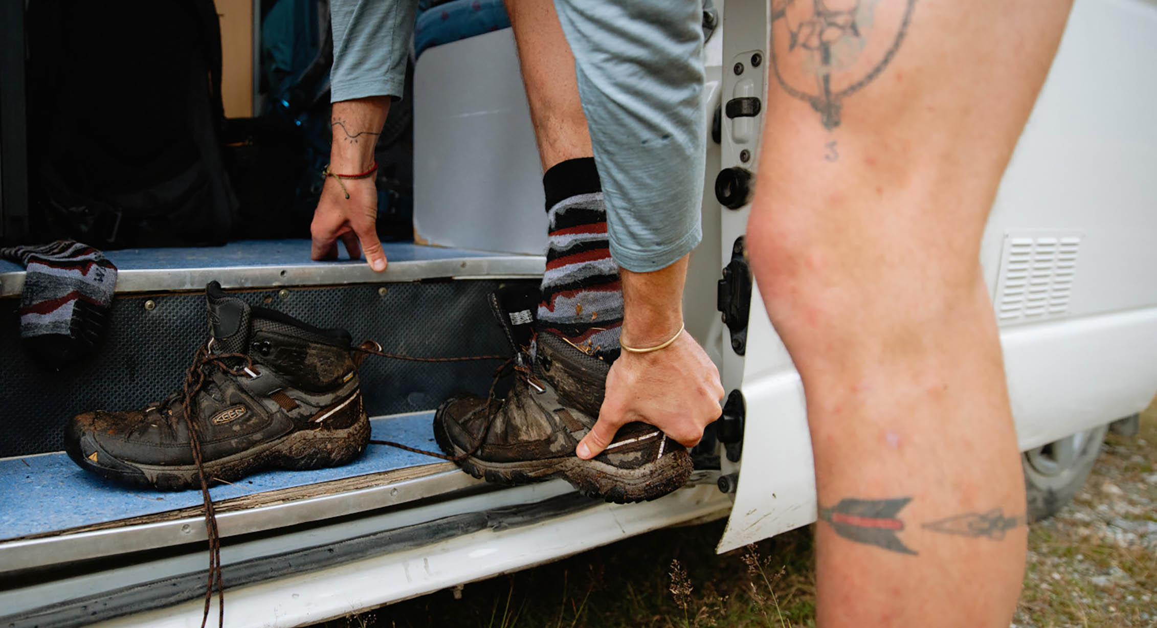 a hiker changes their shoes near a van