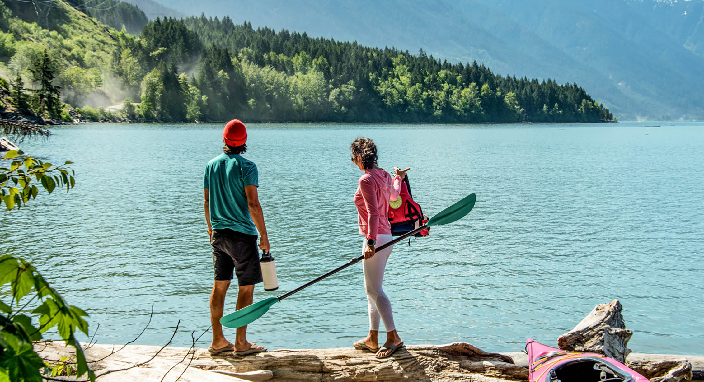 two people get ready to kayak on a quiet lake on a sunny day