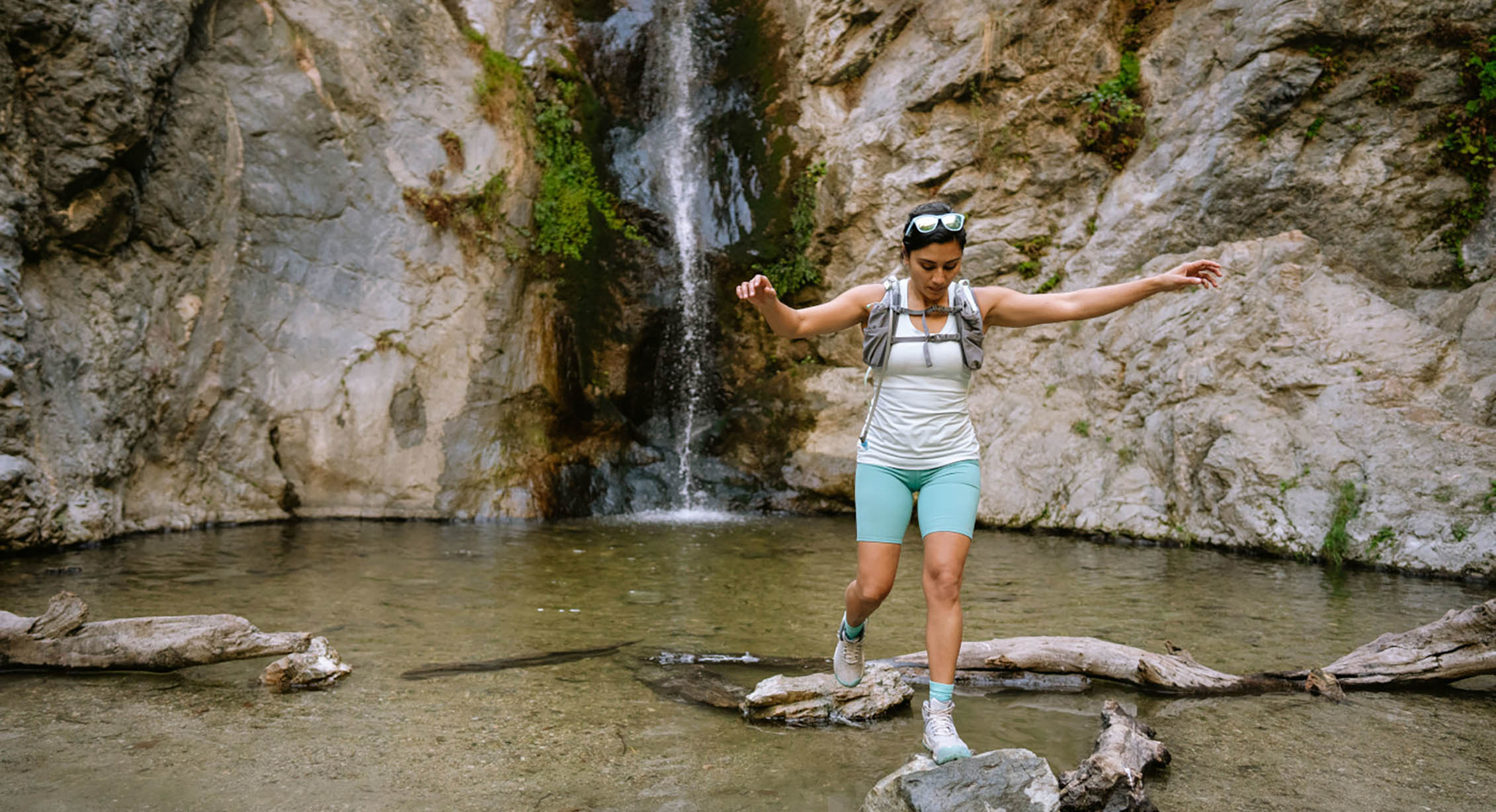 a person hops across rocks while crossing a stream