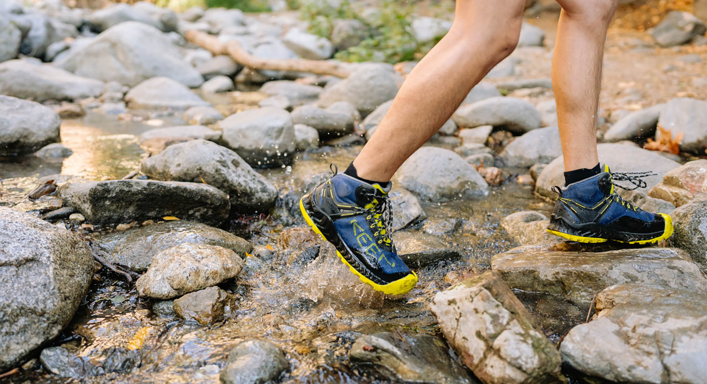 a hiker crosses a flowing stream